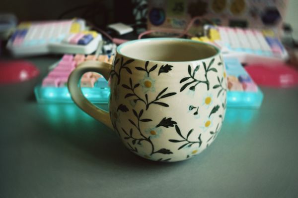 A cream coloured mug with green vines all over and small daisies painted on it.